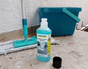 Eine Flasche Bodenreiniger steht vor einem Wischmopp und Eimer.