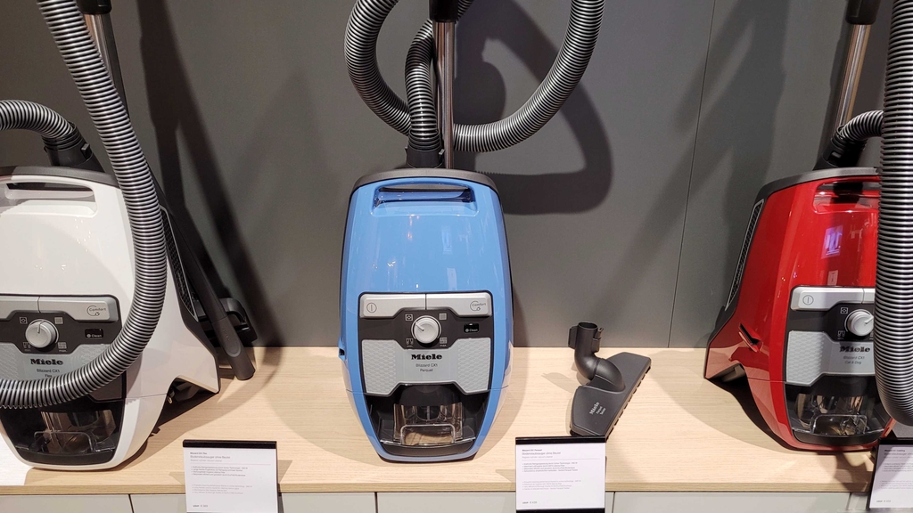 Verschiedene Bodenstaubsauger in verschiedenen Farben sind nebeneinander in einem Verkaufsregal aufgestellt.