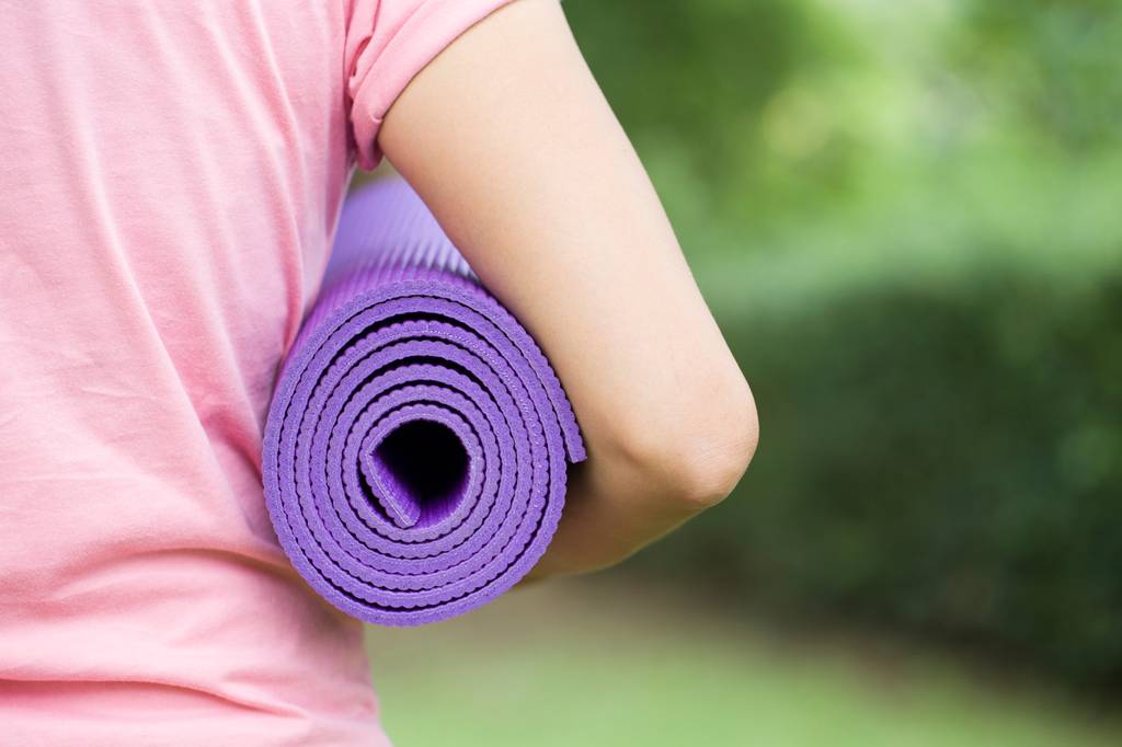 Bodhi-Yogamatte-Test: Eine Frau hält eine lilafarbene Yogamatte unter Ihrem Arm. 