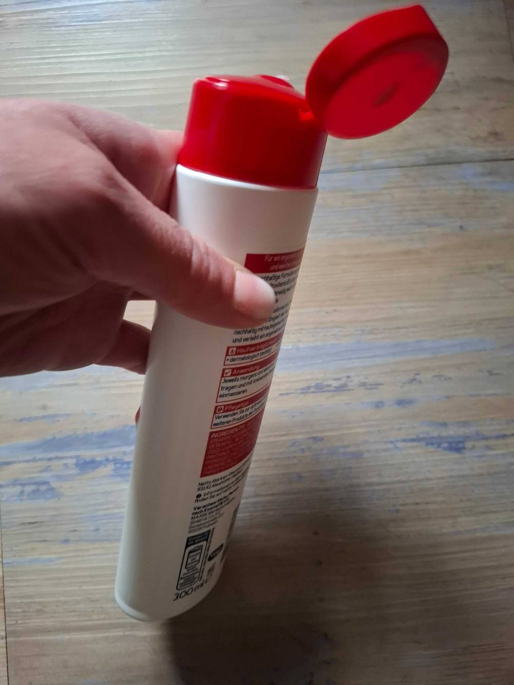 Eine Flasche der getesteten Bodylotion ohne Parfüm von der Seite mit geöffnetem Deckel von einer Hand gehalten.