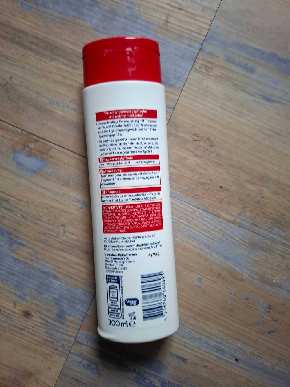 Eine Flasche der Bodylotion ohne Parfüm im Test mit der Rückseite nach oben auf einem Holzboden liegend.
