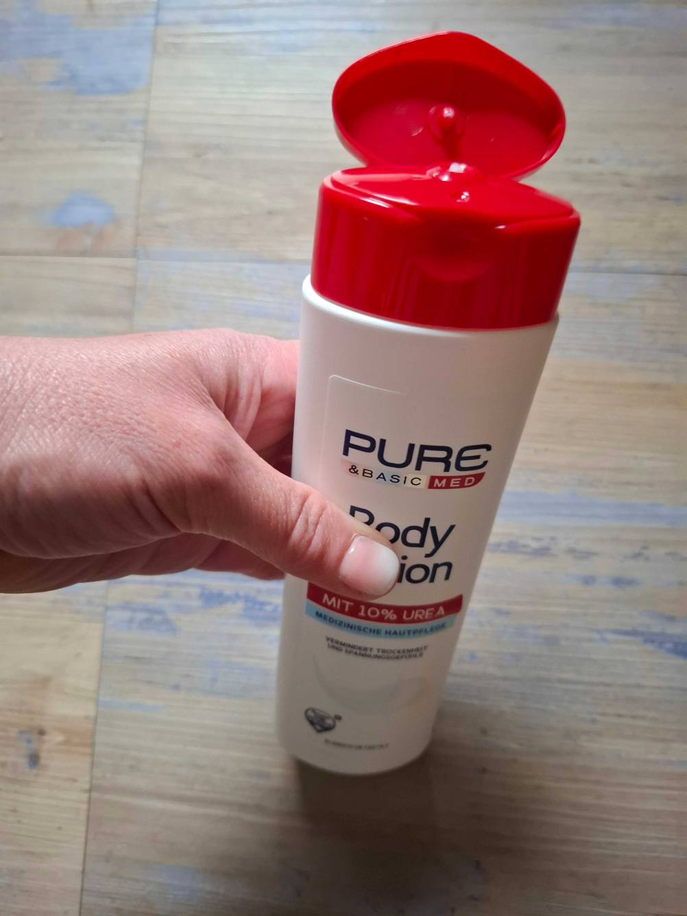 Eine Flasche der getesteten Bodylotion ohne Parfüm mit geöffnetem Deckel, von einer Hand gehalten.