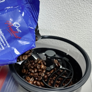 Frische Kaffeebohnen werden in das Bohnenfach der Siemens EQ.6 Plus s700 (TE657503DE) eingefüllt. Das Mahlwerk ist offen sichtbar.