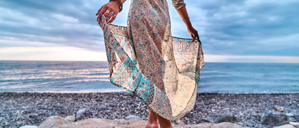 Boho-Kleid im Test: Frau trägt Maxikleid mit Muster und steht am Kiesstrand