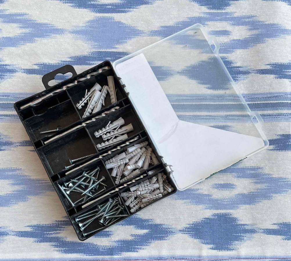 Bohrer-Set getestet: Eine Box mit Schrauben, Bohrern und Dübeln auf einer blau-weißen Tischdecke.