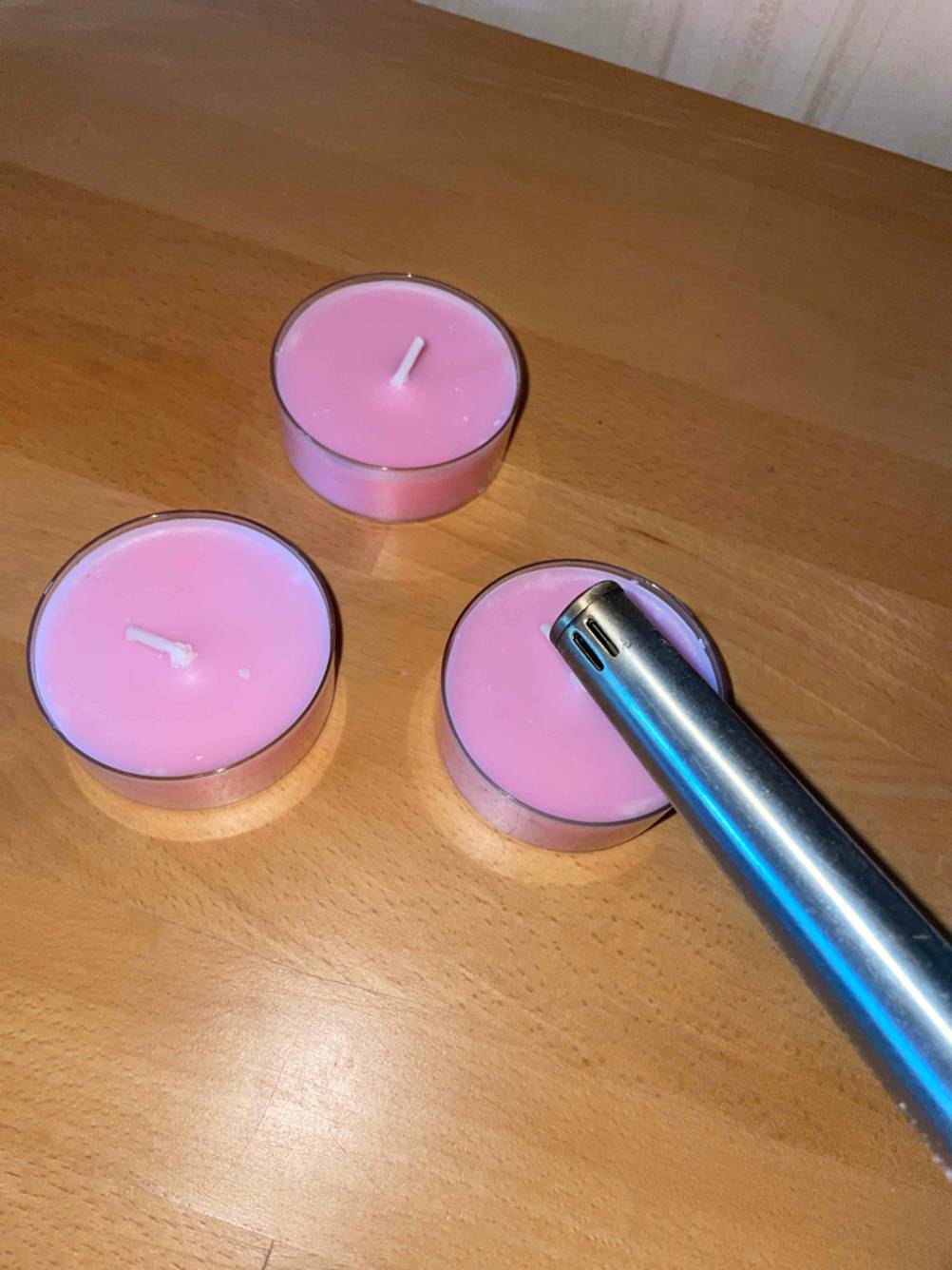 Duftkerzen-Test: Ein Stabfeuerzeug liegt neben drei runden, rosa Duftkerzen.
