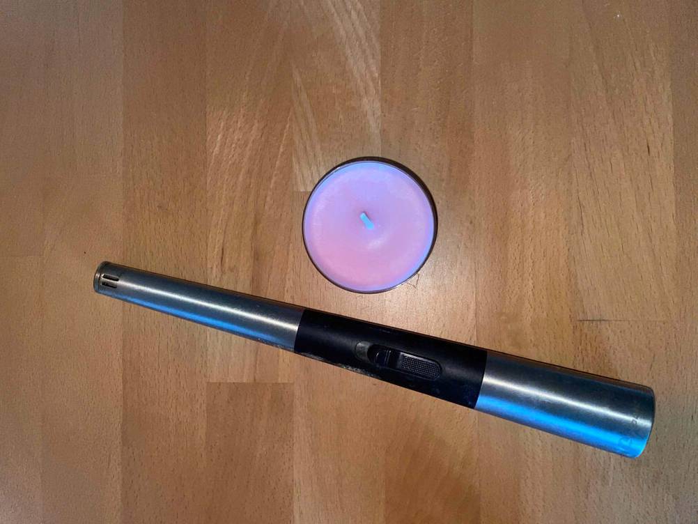 Eine getestete Duftkerze befindet sich auf einer Holzoberfläche neben einem Stabfeuerzeug.