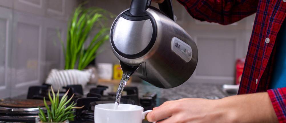Bestron Wasserkocher Test: Person gießt Wasser aus dem Wasserkocher in eine Tasse ein.