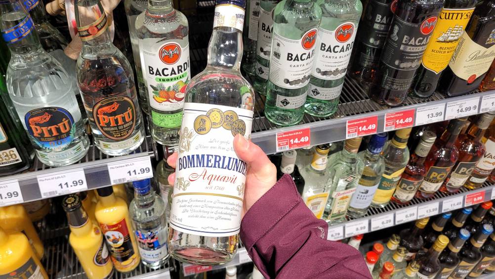 Im Test: Eine Hand hält eine Flasche Aquavit vor ein Regal mit Spirituosen.