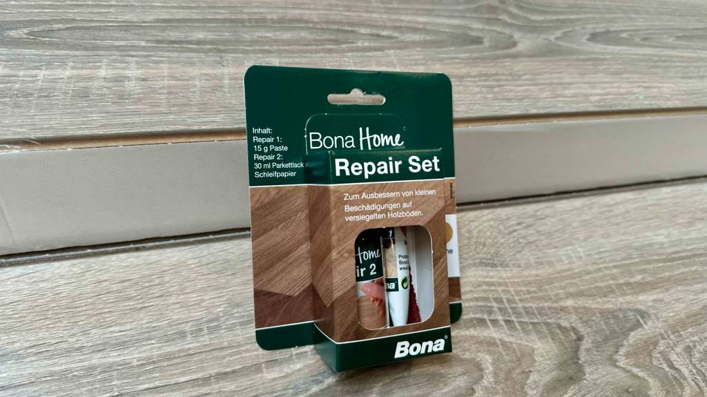 Ein verpacktes Parkett-Reparaturset liegt zum Testen auf einem hellen Holzboden.