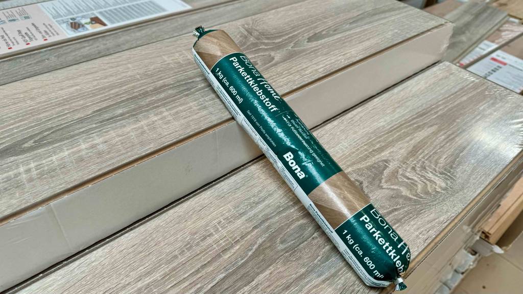 Ein verpackter Parkettkleber liegt zum Testen quer auf hellen Parkettpanels.