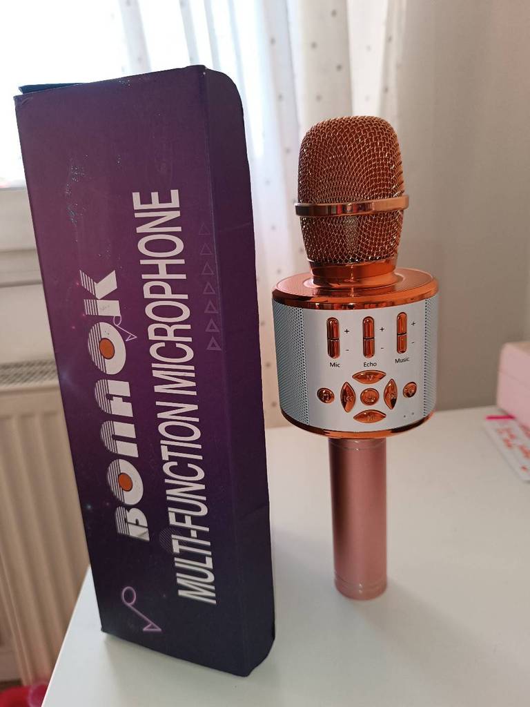 Karaoke-Anlagen im Test: Ein Karaoke-Mikrofon im Kupfer-Design der Marke Bonaok steht neben seiner violetten Originalverpackung auf einer weißen Fläche.