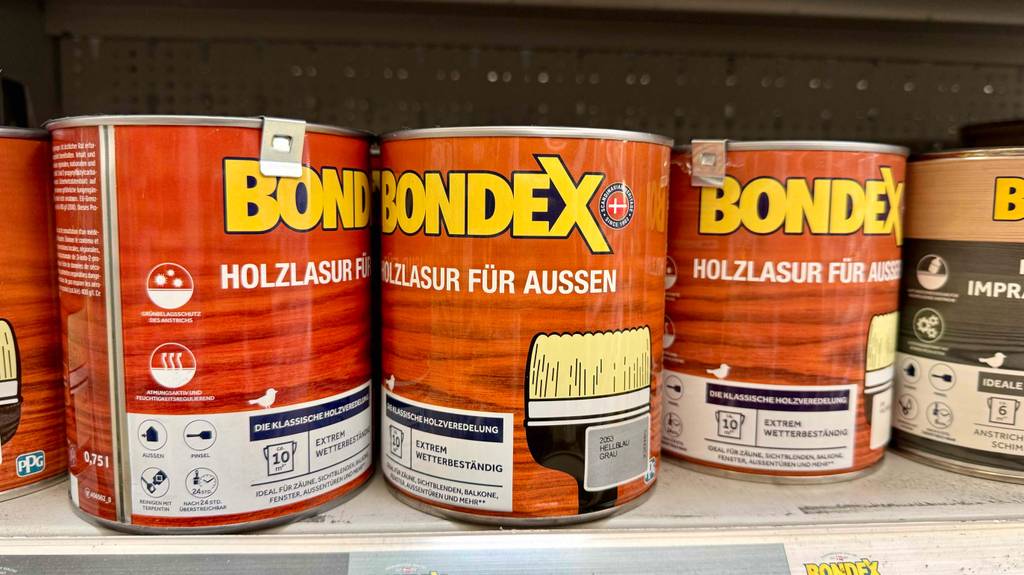 Holzlasur grau im Test: Mehrere Dosen stehen nebeneinander in einem Regal.