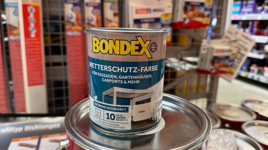 Die getestete weiße Wetterschutzfarbe in der Dose, ausreichend für sieben Quadratmeter, steht auf einem größeren Gebinde mit Farbe.