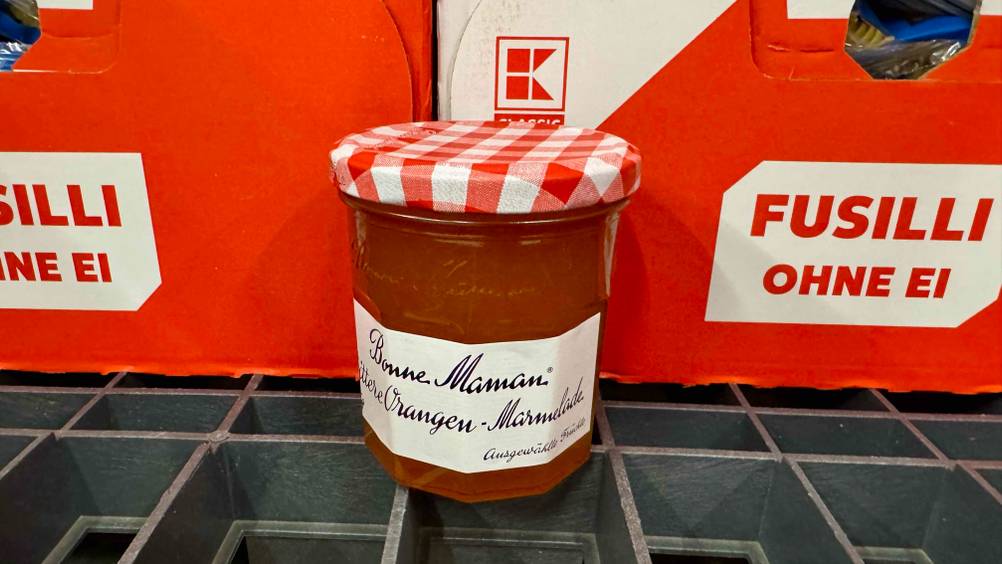 Ein Glas der getesteten Bonne-Maman-Marmelade von schräg oben vor roten Kartons.