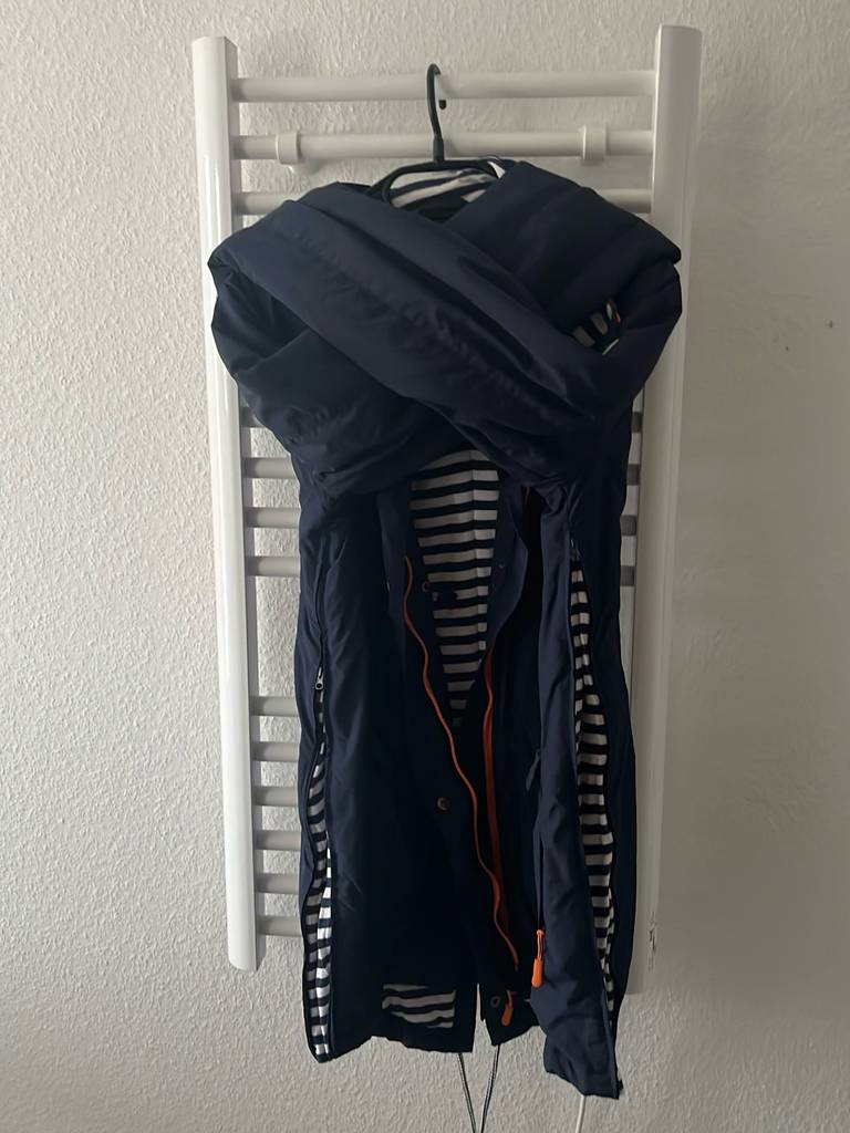 Getestet: eine Damen-Tragejacke mit Babyeinsatz hängt auf einem Kleiderbügel an einer Wandheizung.