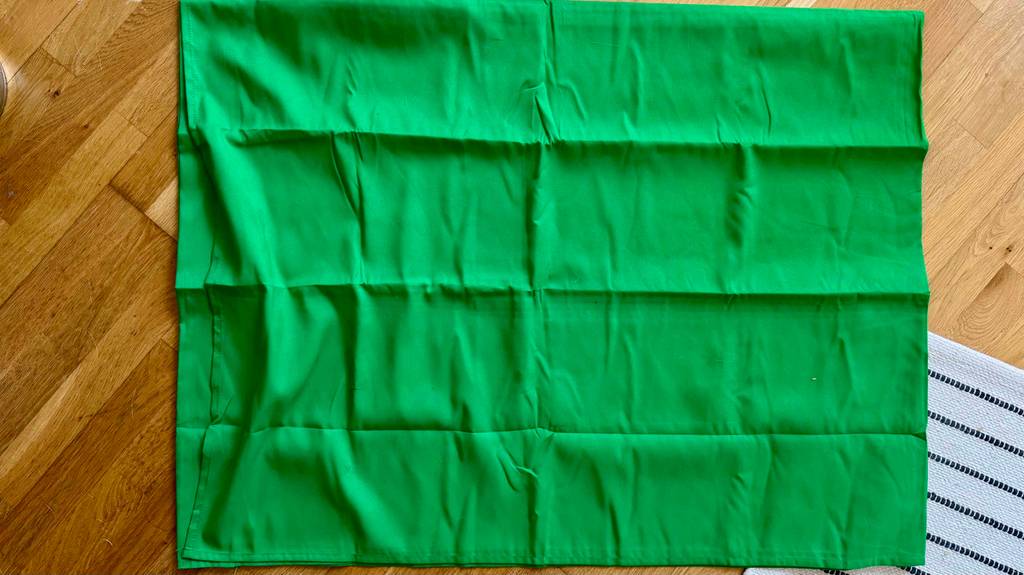Ein ausgebreiteter Green Screen im Test liegt auf einem Laminatboden.