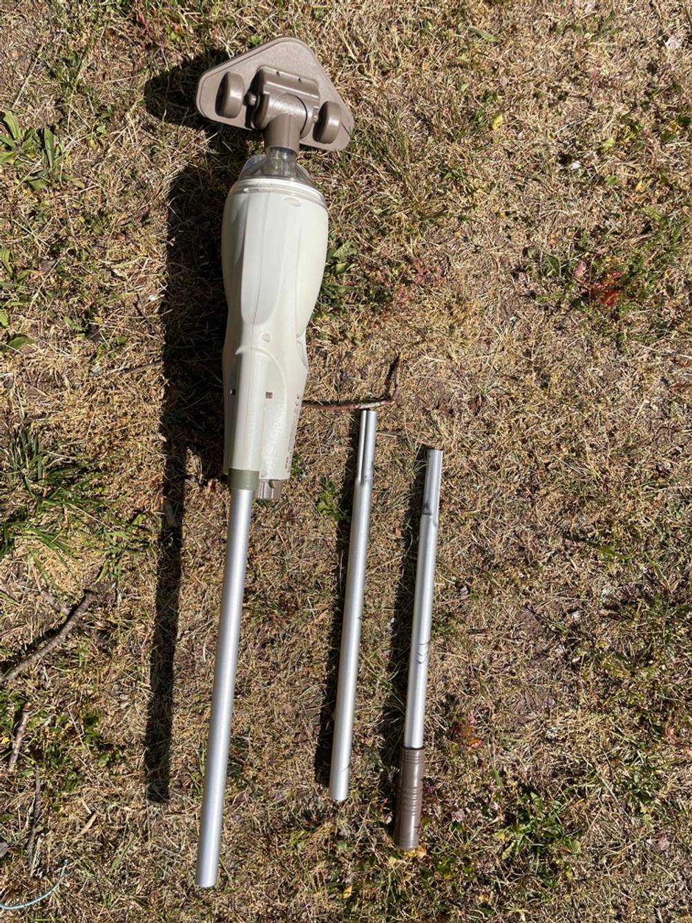 Ein getesteter Akku-Poolsauger mit auseinandergebauter Stange auf einer Wiese liegend.