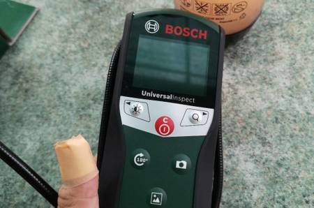 Getestete Endoskop-Kamera 603687000 von Bosch in einer linken Hand vor einer grünlichen Tischfläche mit Wasserflaschen.