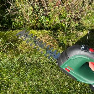 Eine Hand schneidet Gras mit der Bosch AdvancedShear 18V-10.