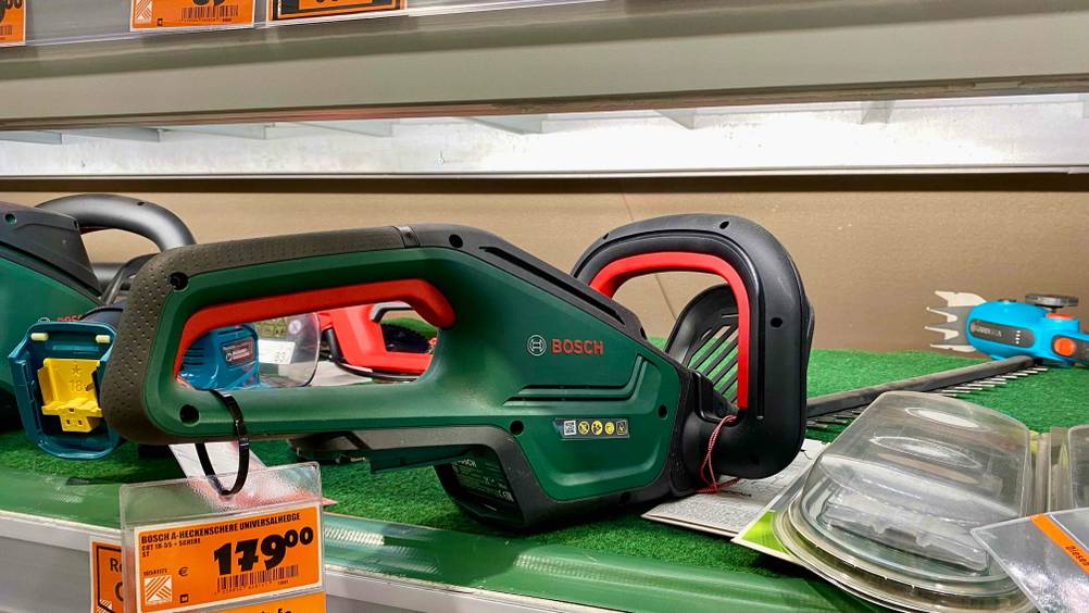 Im Test: Nahaufnahme des Griffes einer Bosch-Akku-Heckenschere mit Preisangabe zwischen anderen Produkten auf einem Regal.