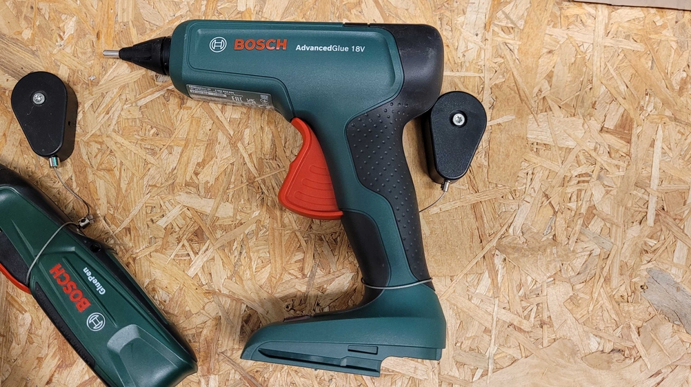 Heißklebepistole mit Zubehörteilen liegt auf einer Holzplatte.