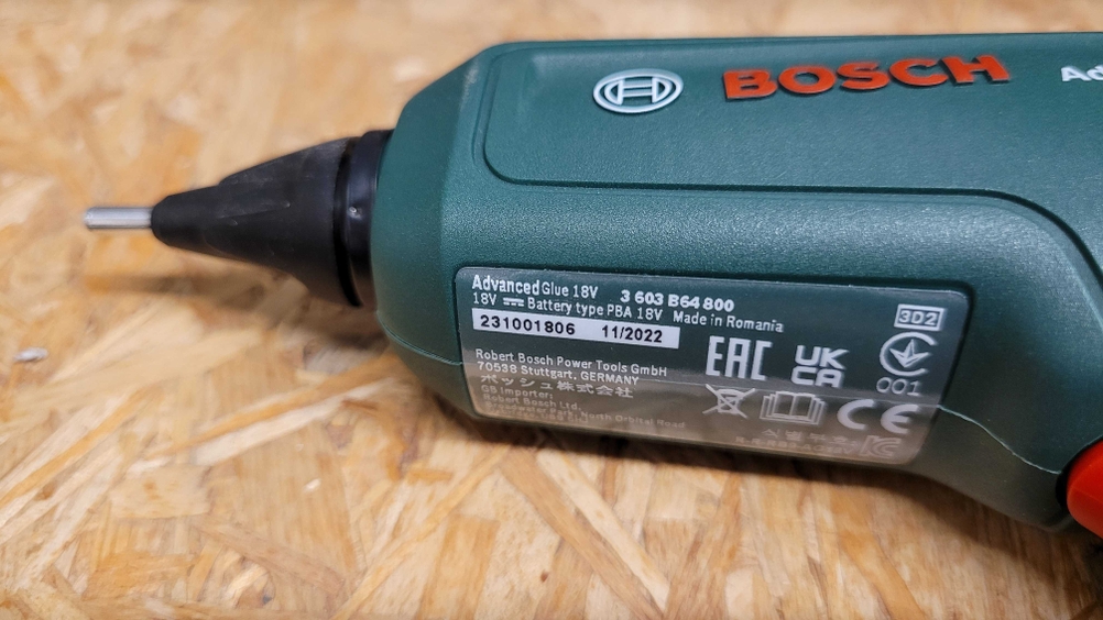 Heißklebepistole liegt seitlich auf einer Holzplatte, das Typenschild ist deutlich sichtbar