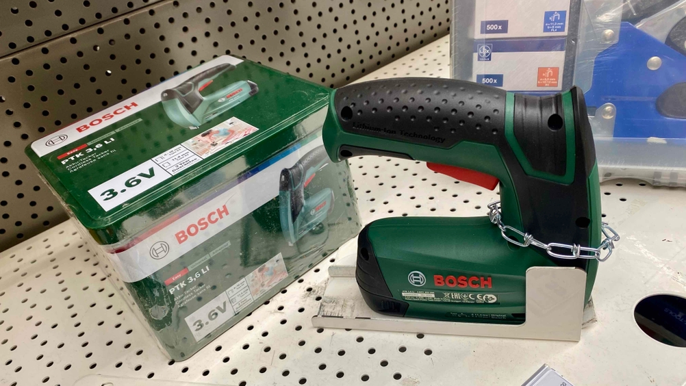 Bosch Akku-Tacker PTK 3.6 LI steht auf einem Ladenregal neben seiner Originalverpackung. Das Gerät ist mit einem Kettensicherungssystem befestigt.