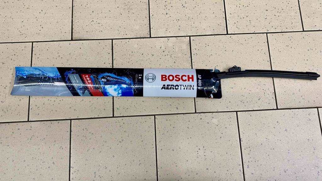 Ein getesteter Scheibenwischer befindet sich in einer blau-weißen Bosch AeroTwin AP 400 U Verpackung halb herausgezogen auf beigefarbenen Fliesen.