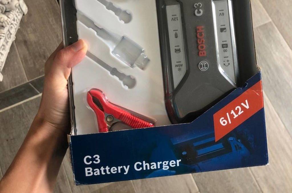 Bosch-C3-Autobatterie-Ladegerät-Test: Hand hält die Originalverpackung inklusive Gerät in einem Wohnbereich.