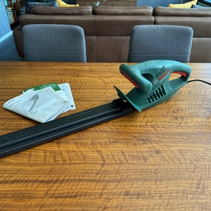 Die Bosch Easy Hedge Cut 45 liegt neben den Anleitungen auf einem Holztisch.