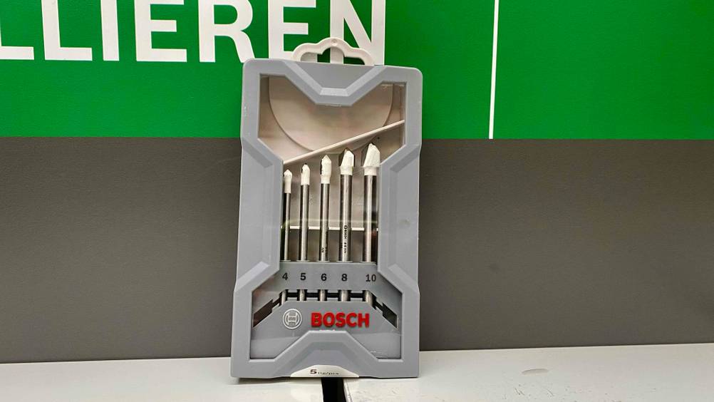 Fliesenbohrer getestet: Ein Set originalverpackter Fliesenbohrer lehnt an einer grau-grünen Wand.