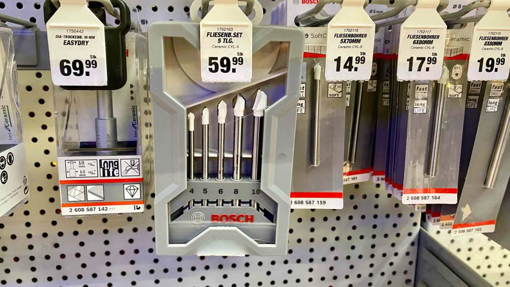 Ein getestetes Set Fliesenbohrer hängt neben anderen Produkten in einem Verkaufsregal mit Preisangaben.