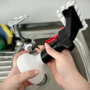 Eine Hand hält die Bosch-GlassVAC-Sprühflasche mit aufgestecktem Mikrofaserwischer. Der Wischer ist grau und breitflächig.