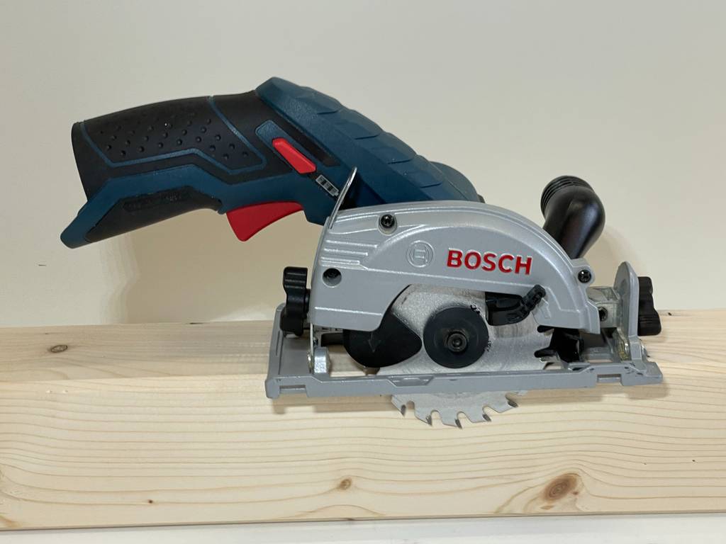 Eine getestete Bosch-Handkreissäge, mit Blick auf das Sägeblatt, befindet sich von der Seite betrachtet auf einem Holzblock.