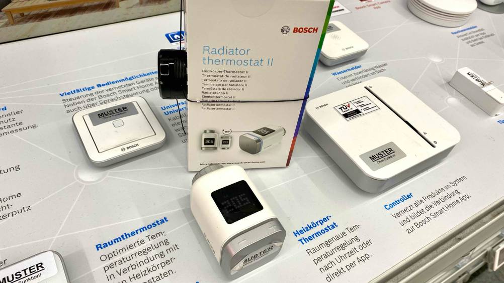 Ein Heizkörperthermostat im Test auf einer Infotafel in einer Ausstellung, daneben die Originalverpackung.