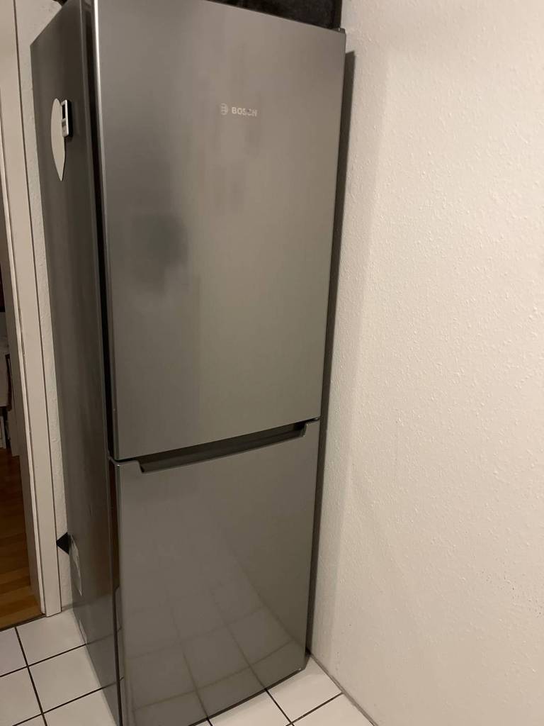 Bosch Kühl-Gefrierkombination im Test: silbernes Modell steht geschlossen auf weißen Fliesen vor weißer Wand.