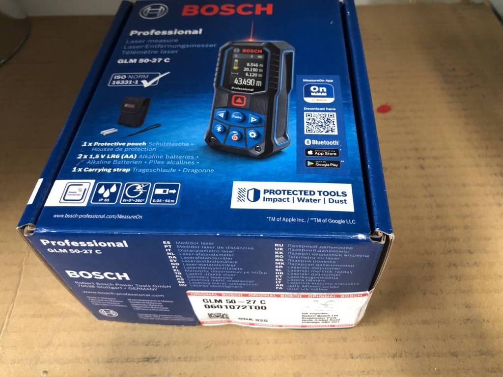 Blaue geschlossene Originalverpackung des Bosch Professional GLM 50-27 C Laser-Entfernungsmessers im Test steht auf einer hellbraunen Fläche.