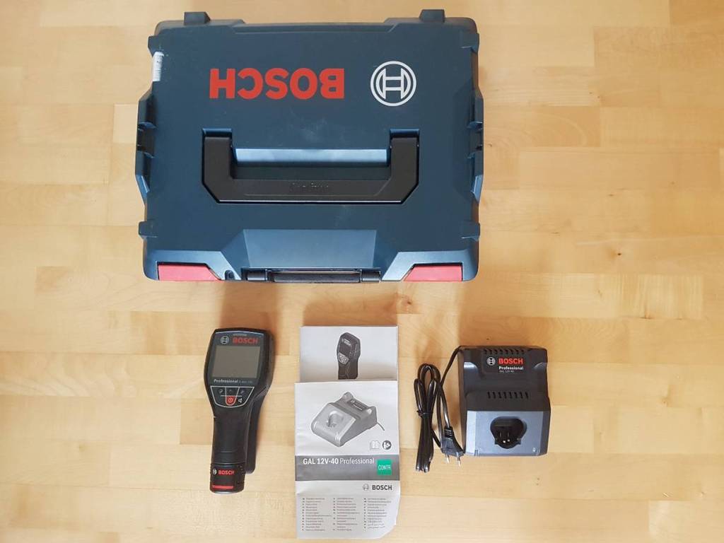 Sicht von oben auf ein getestetes Wärmebildkamera-Set der Marke Bosch inklusive Ladestation, Transportkoffer und Bedienungsanleitung auf einem Holzboden.