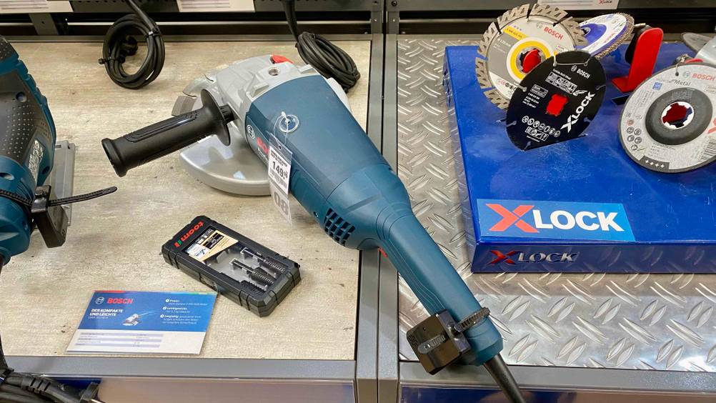 Ein getesteter Winkelschleifer-230-mm von schräg oben zwischen anderen Produkten in einem Verkaufsregal liegend.