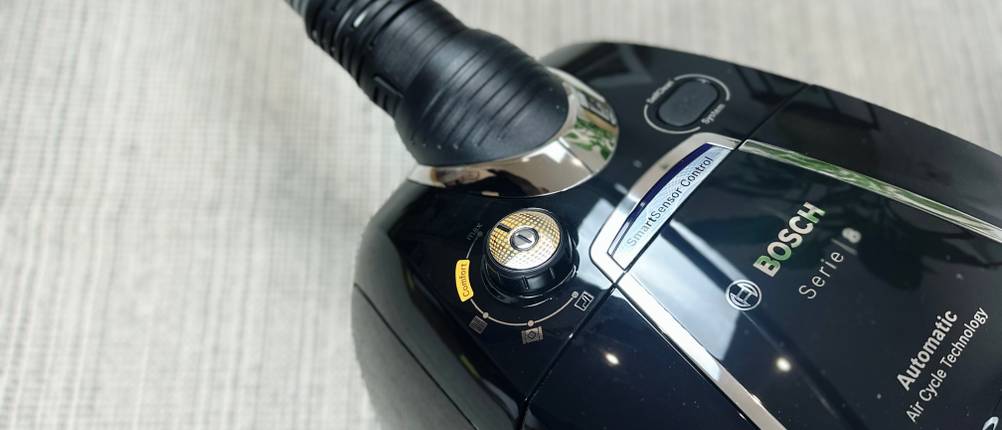 Der Bosch ProSilence Serie 8 BGS7MS64 ist auf einem Teppichboden zu sehen. Der Staubsauger steht aufrecht mit angeschlossenem Saugrohr und montierter Bodendüse.