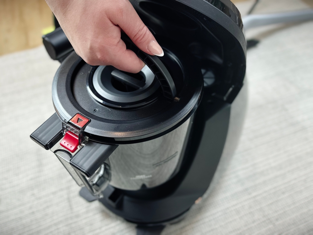 Eine Hand entnimmt den Staubbehälter aus dem Bosch ProSilence Serie 8 BGS7MS64. Der Behälter befindet sich unter der geöffneten Gehäuseklappe.