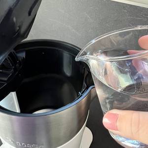 Wasser mit Messbecher in Wasserkocher eingießen