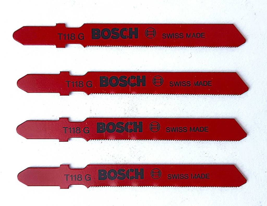 Vier Stichsägeblätter Metall liegen in Reihe übereinander zum testen auf einer weißen Fläche.