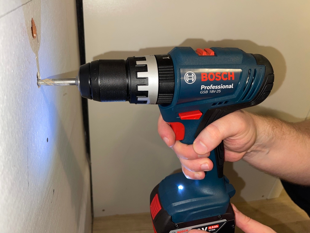 Die Bosch GSB 18V-25 Professional beim Bohren in eine weiße Wand. Bohrer ist im Material angesetzt.