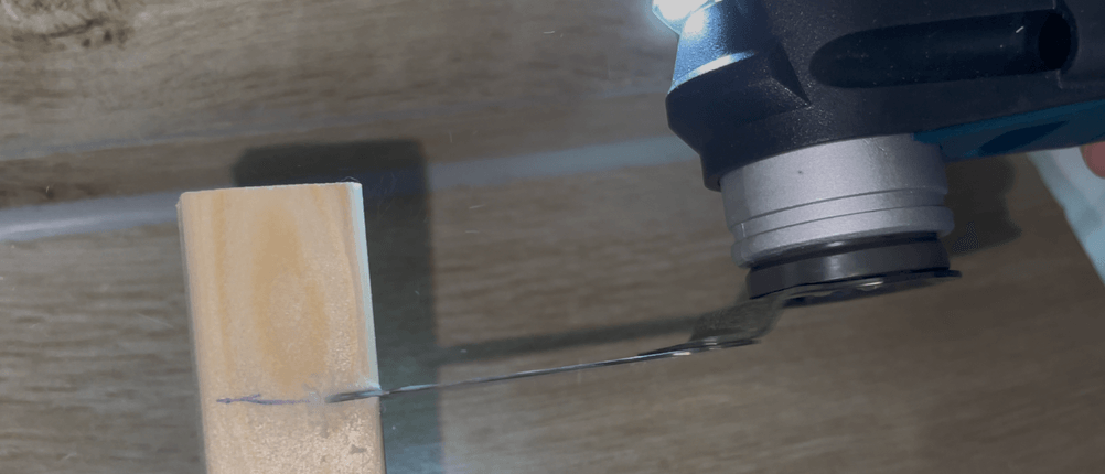 Das Bosch GOP 40-30 wird genutzt, um ein Holzstück entlang einer Markierung zu durchtrennen. Die integrierte LED-Leuchte ist eingeschaltet.