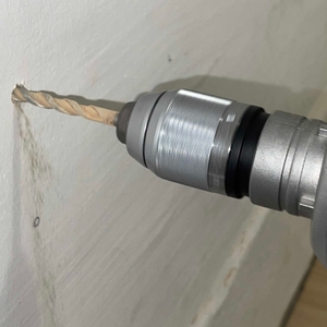 Seitenansicht des Bohrers der Bosch GSB 21-2 RCT beim Austritt aus der Wand, sichtbare Staubentwicklung.