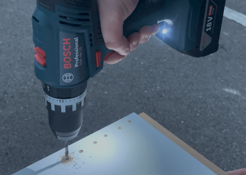 Die Bosch GSB 18V-25 Professional beim Bohren in eine Holzplatte im Freien, Lichtverhältnisse eher dunkel.