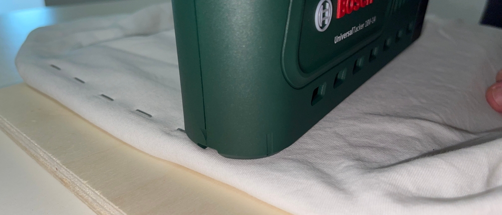 Der Bosch UniversalTacker 18V‑14 wurde mehrfach in eine Stoff-Holz-Kombination ausgelöst. Die Klammern verlaufen gleichmäßig in einer Linie.