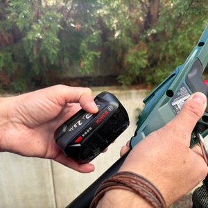 Eine Hand steckt den Akku an die Bosch Universal HedgePole 18